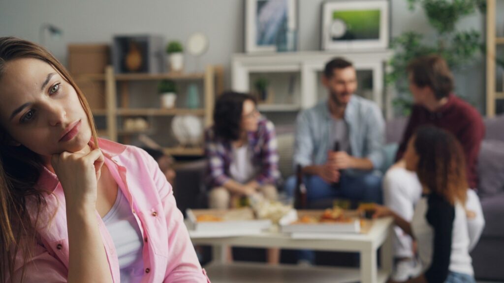 Mulher com ansiedade social, pensativa e isolada em meio a um grupo de amigos.